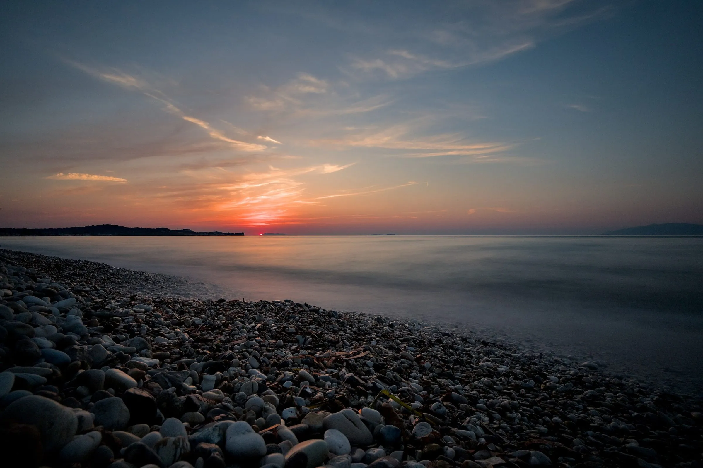 Sonnenuntergang über dem Meer am Kiesstrand von Acharavi